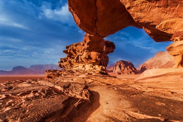 Natural rock arch formation in Wadi Rum desert landscape with red sandstone cliffs and blue sky in Jordan